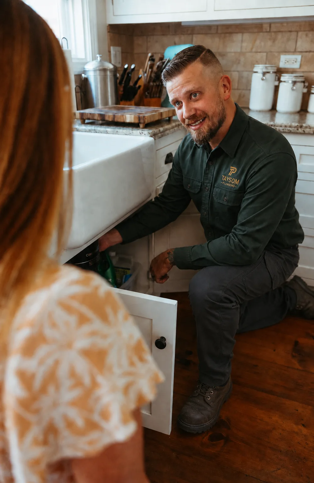 Eric Taysom under a kitchen sink, talking a homeowner through what he found